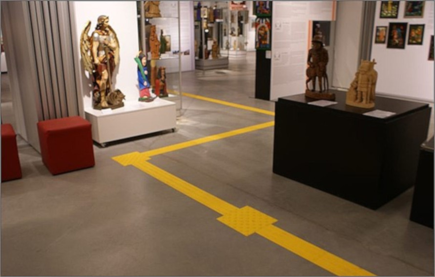 żółta, wypukła ścieżka prowadząca pomiędzy eksponatami na wystawie w muzeum